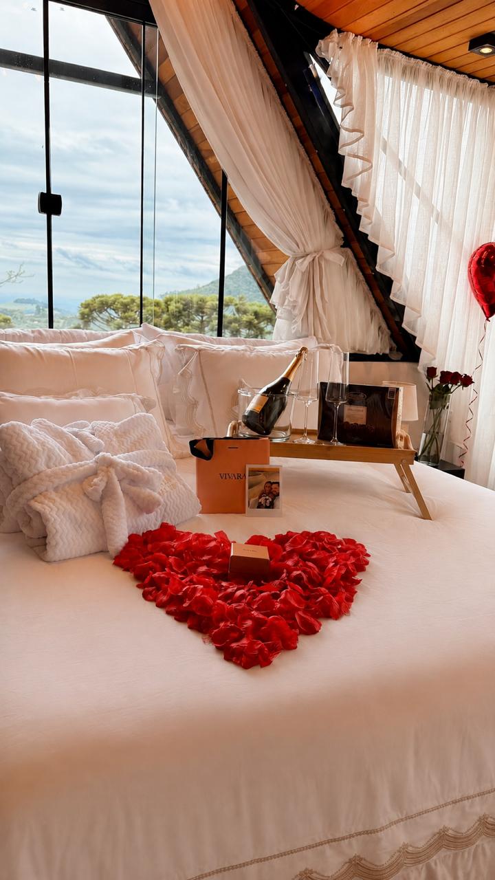 Cama decorada com pétalas em formato de coração, espumante e roupões